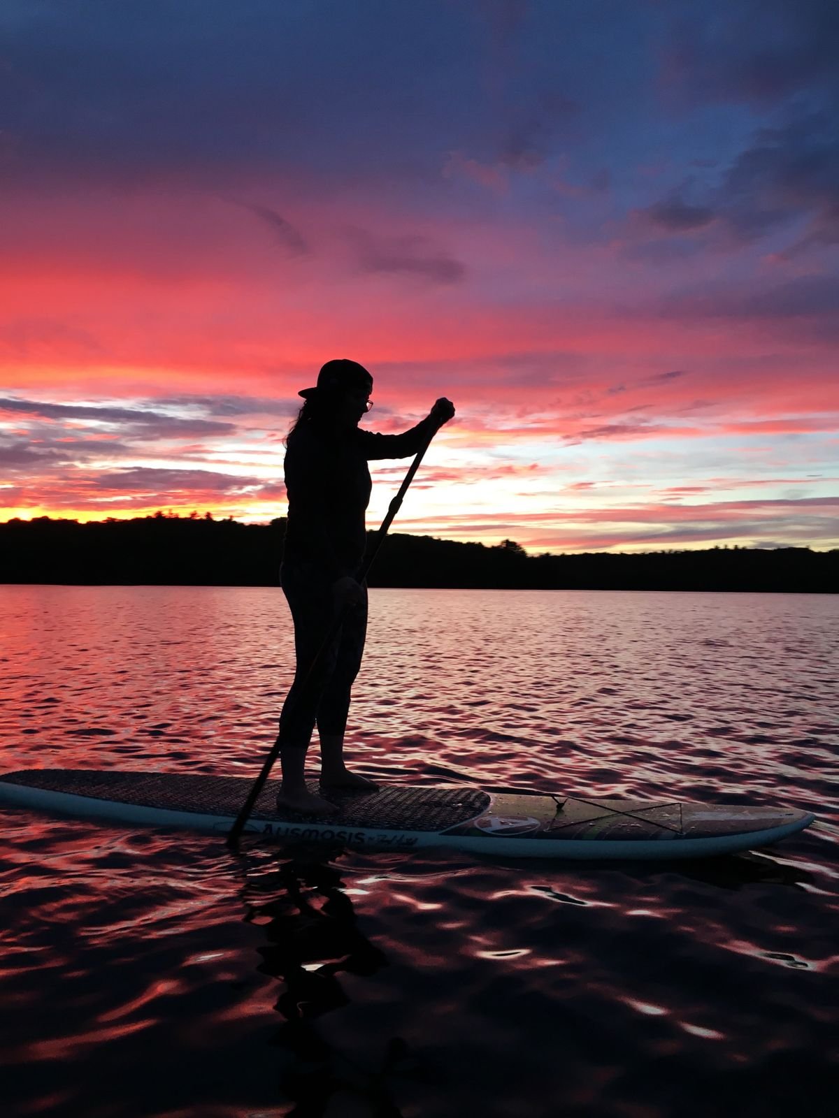 Silueta de una persona remando de pie en una tabla de paddle surf con el cielo naranja de fondo
