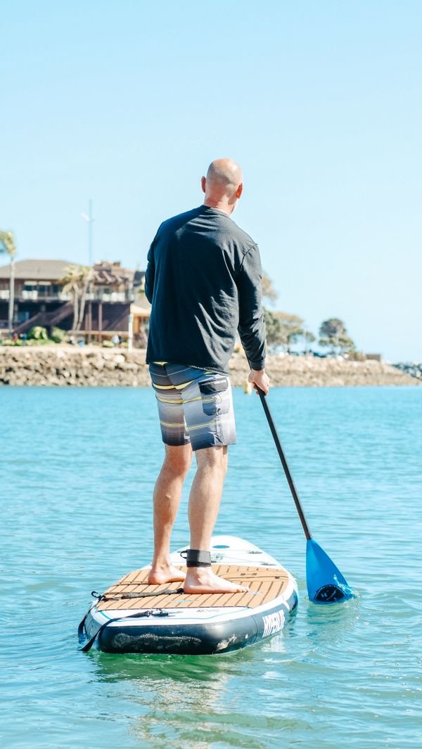Hombre sonriente remando de pie en una tabla de paddle surf en el mar